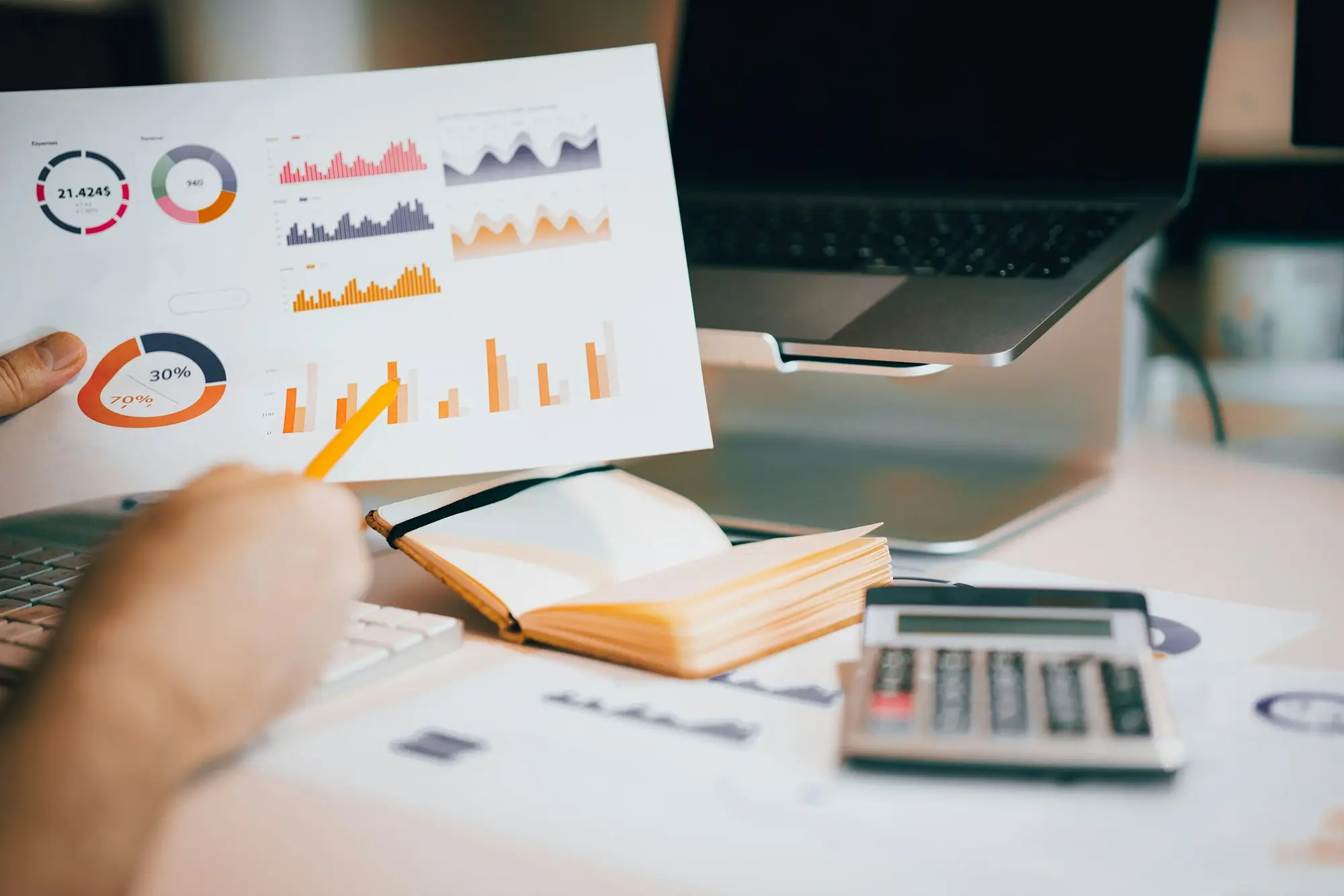 Person holding a printed financial report with charts while reviewing figures on a laptop