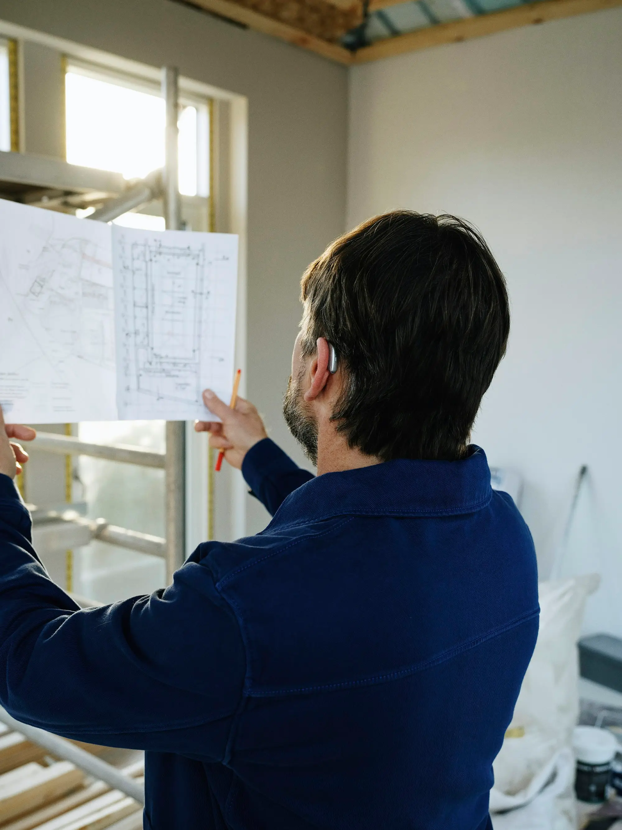 Builder reviewing architectural plans with a pencil on a residential construction site