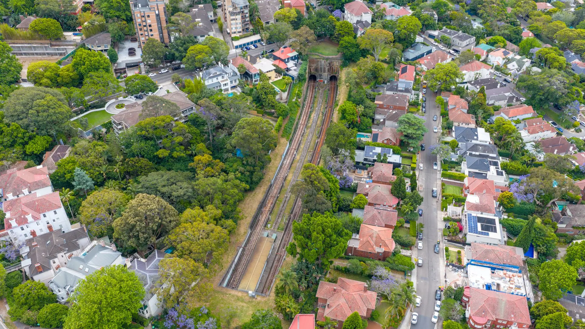 Aerial view of a leafy Sydney suburb with red-roofed houses and apartment blocks either side of a railway cutting