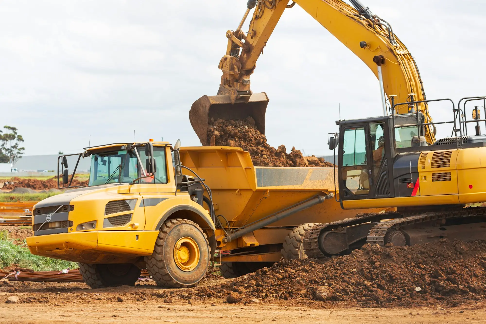 Excavator loading soil into a dump truck during early earthworks on a cleared development site