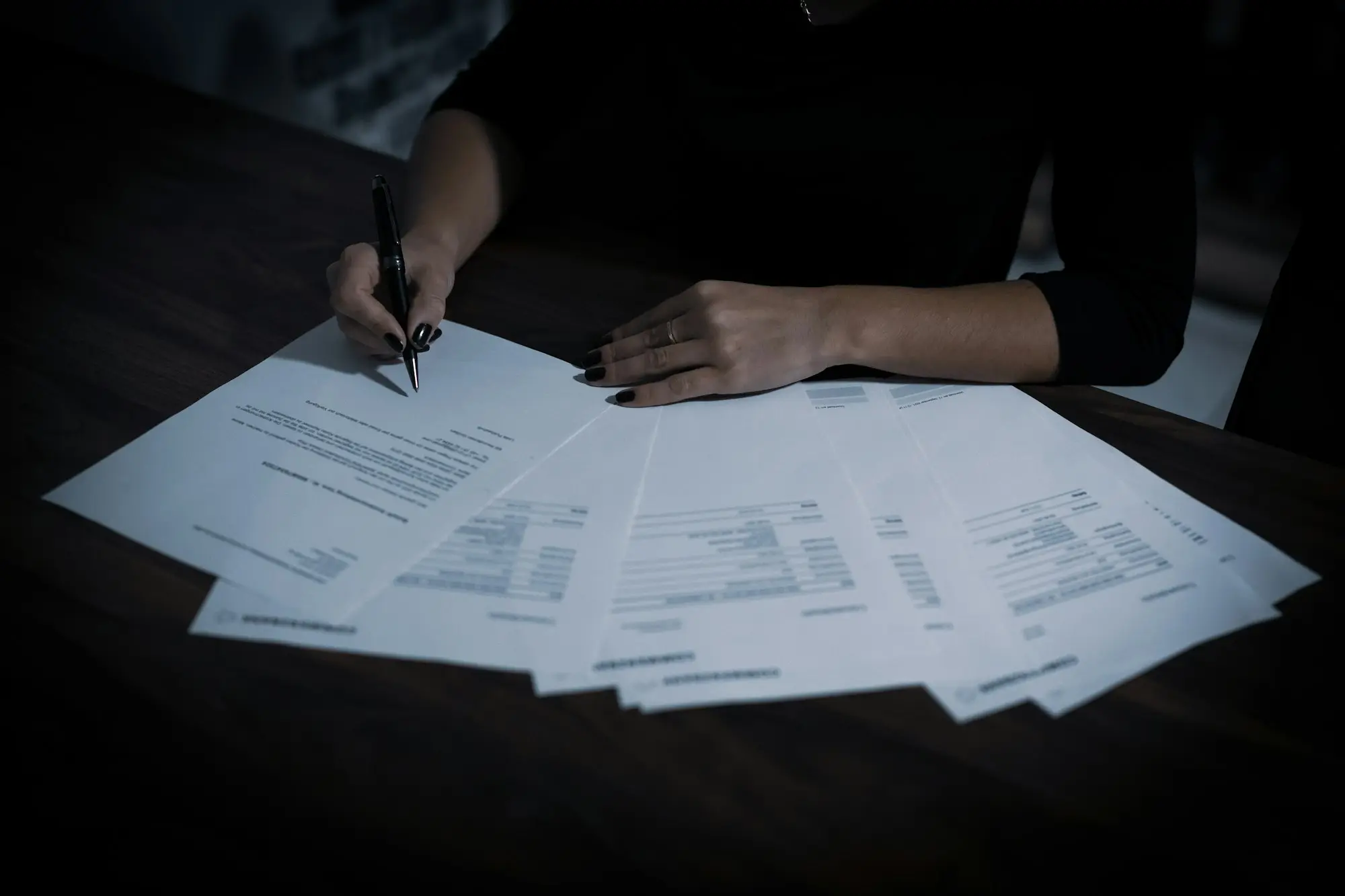 Woman working through a pile of tax paperwork and signing documents at a table