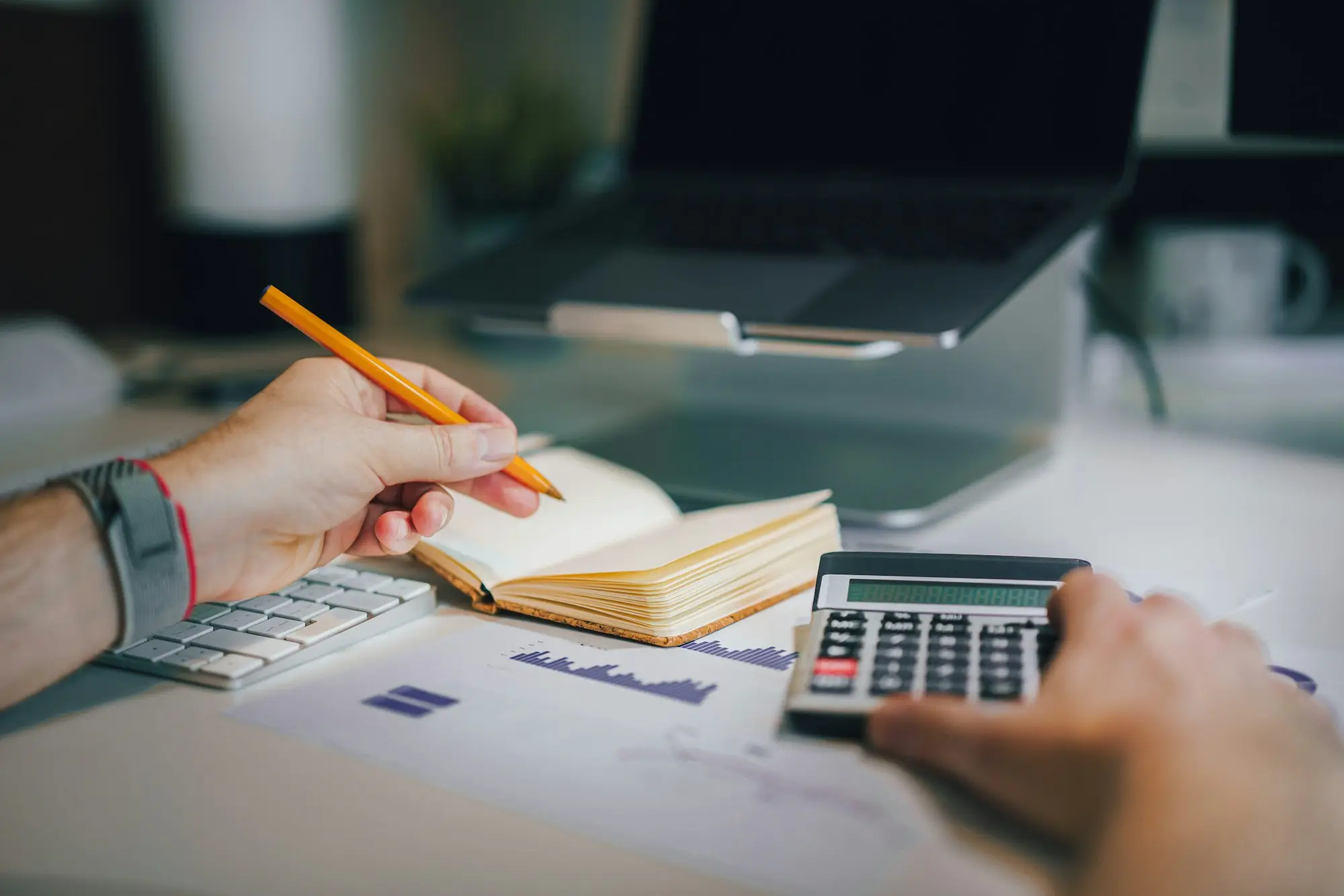 Person at a desk working through costs with a calculator and an open notebook