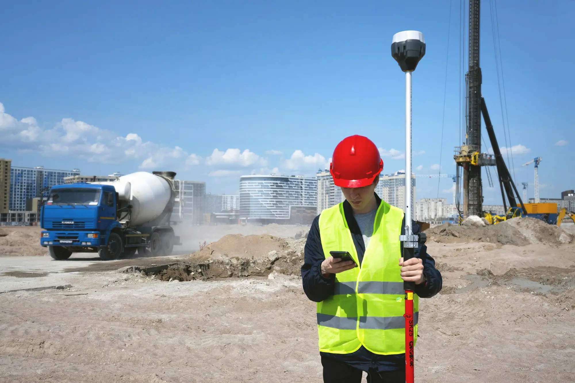 Surveyor in a hard hat and hi-vis jacket taking GNSS positioning readings on a construction site