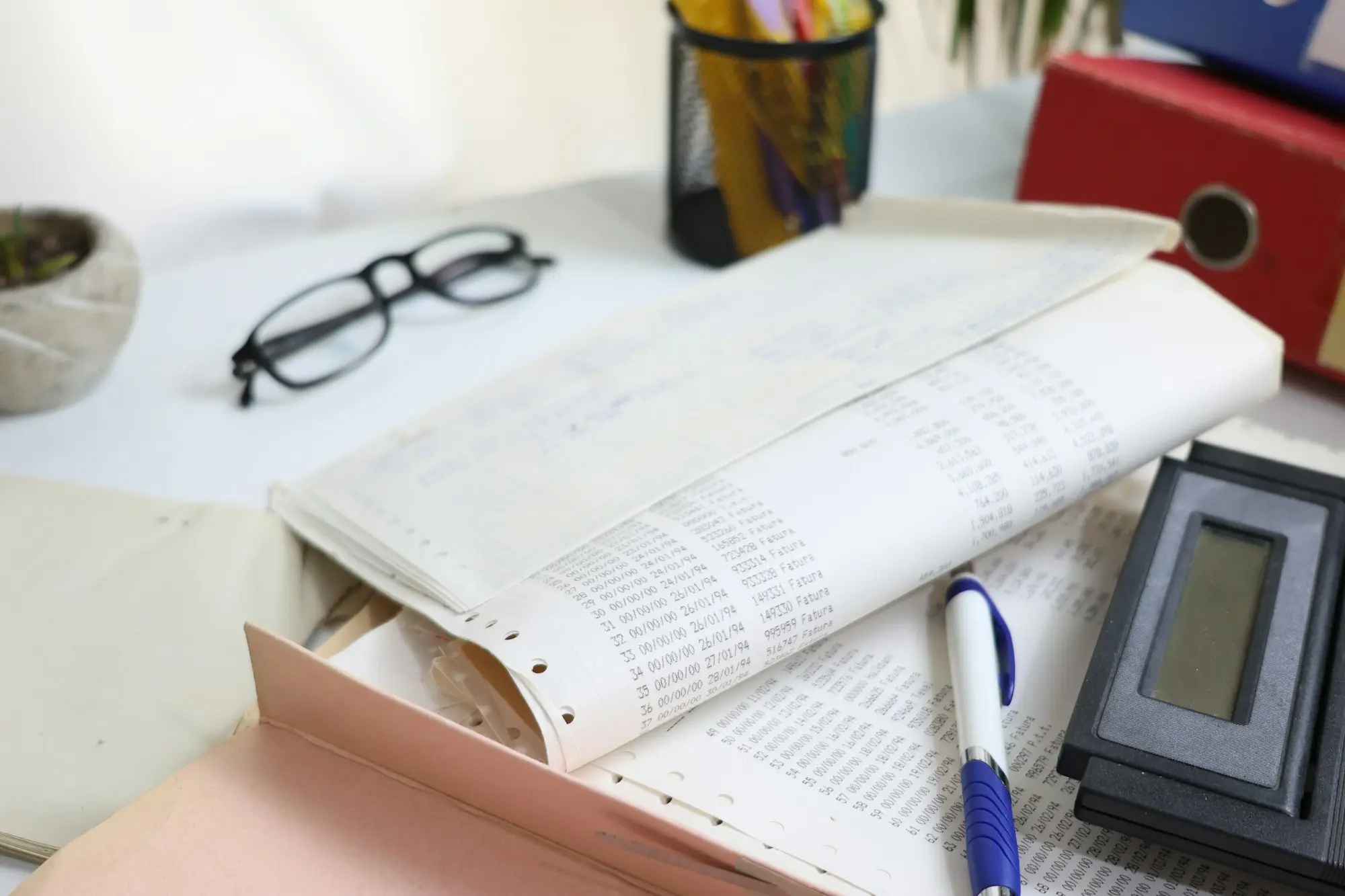 Desk covered in receipts, papers, glasses and a calculator ready for record keeping