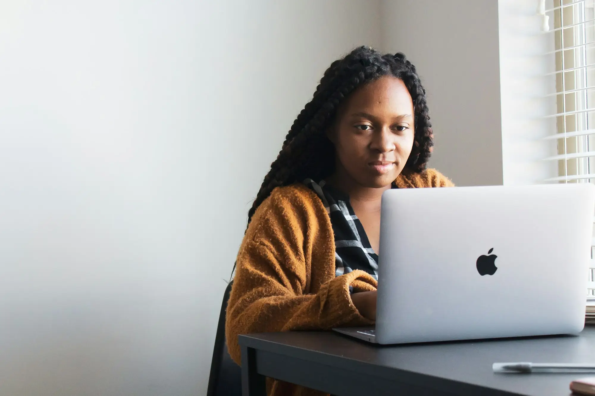 Woman researching on a laptop at her desk in a calm, well-lit home workspace