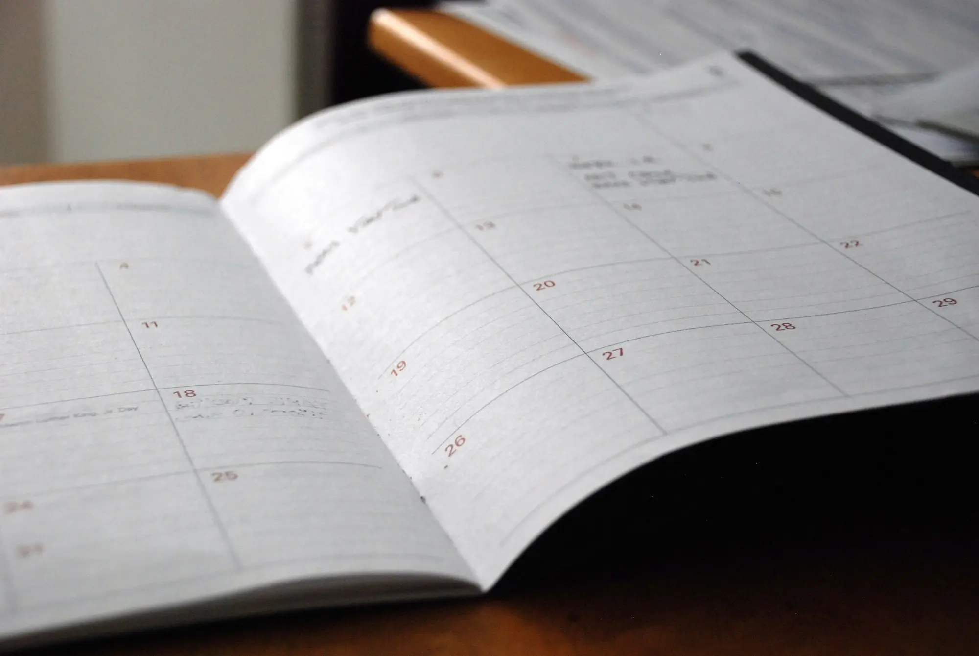 Open monthly planner on a wooden desk showing a calendar grid of upcoming dates