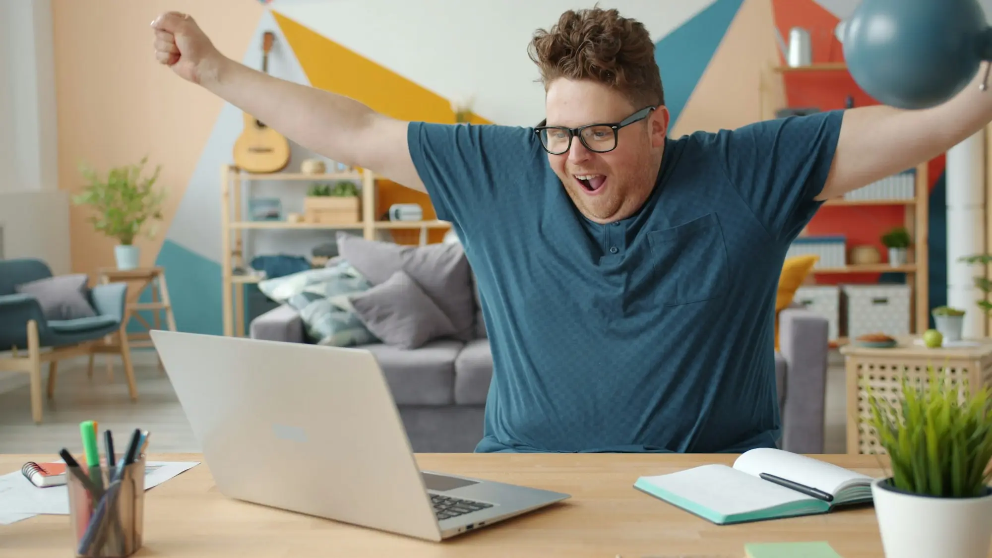 Relieved businessman raising his arms in celebration while working on a laptop at home