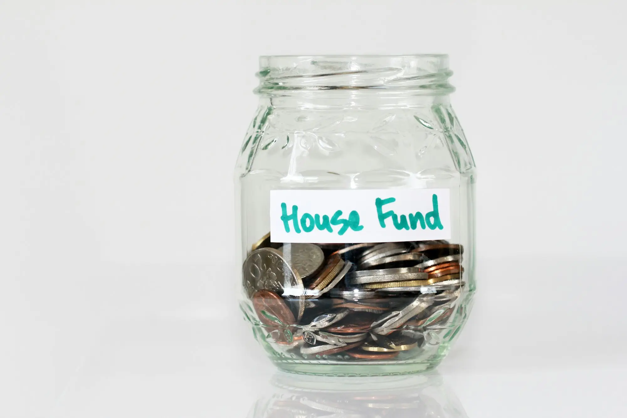 Glass jar filled with coins and labelled house fund, a reminder to budget every cost