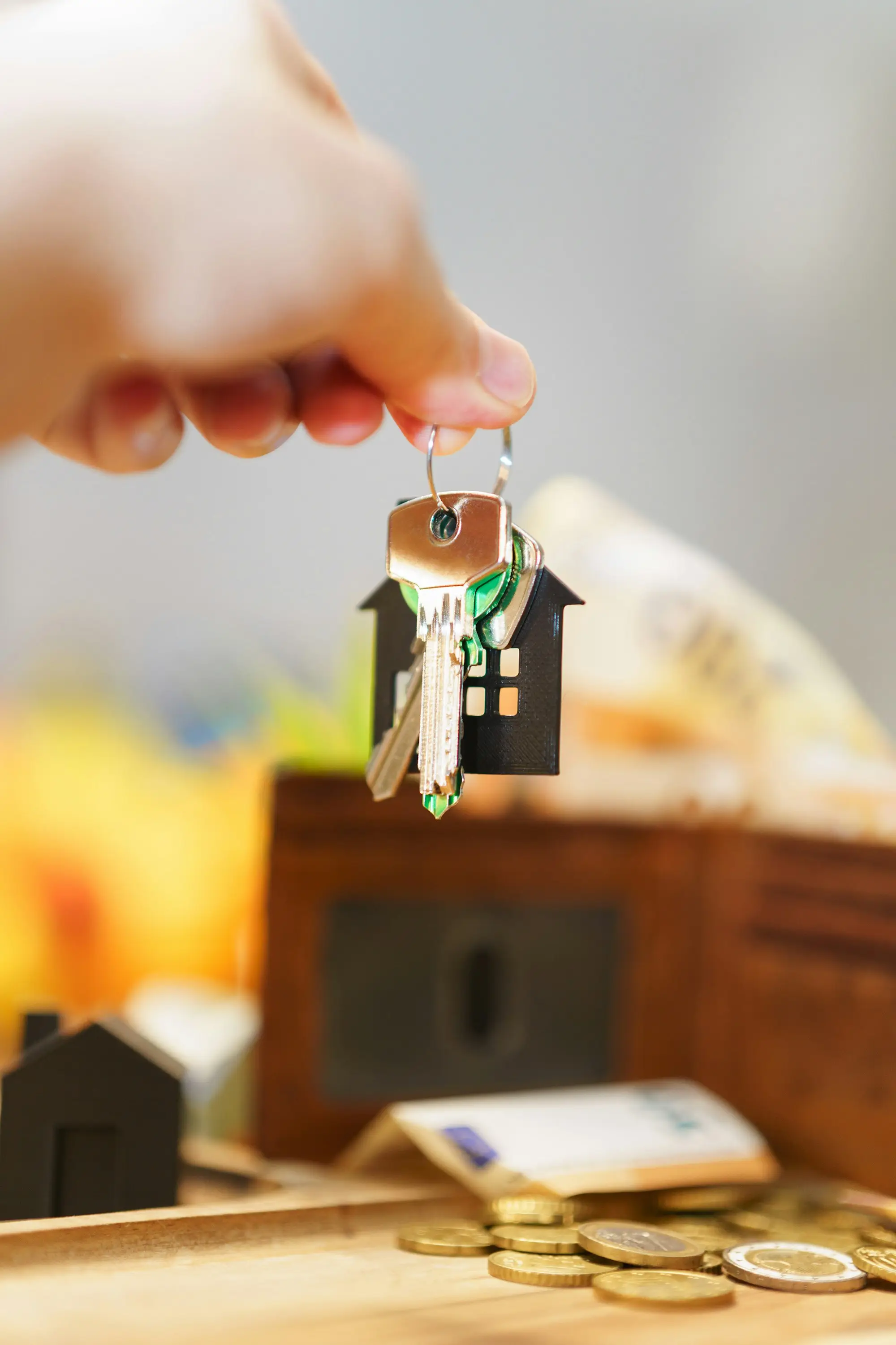 Hand holding new house keys on a house-shaped keyring above coins and a wallet
