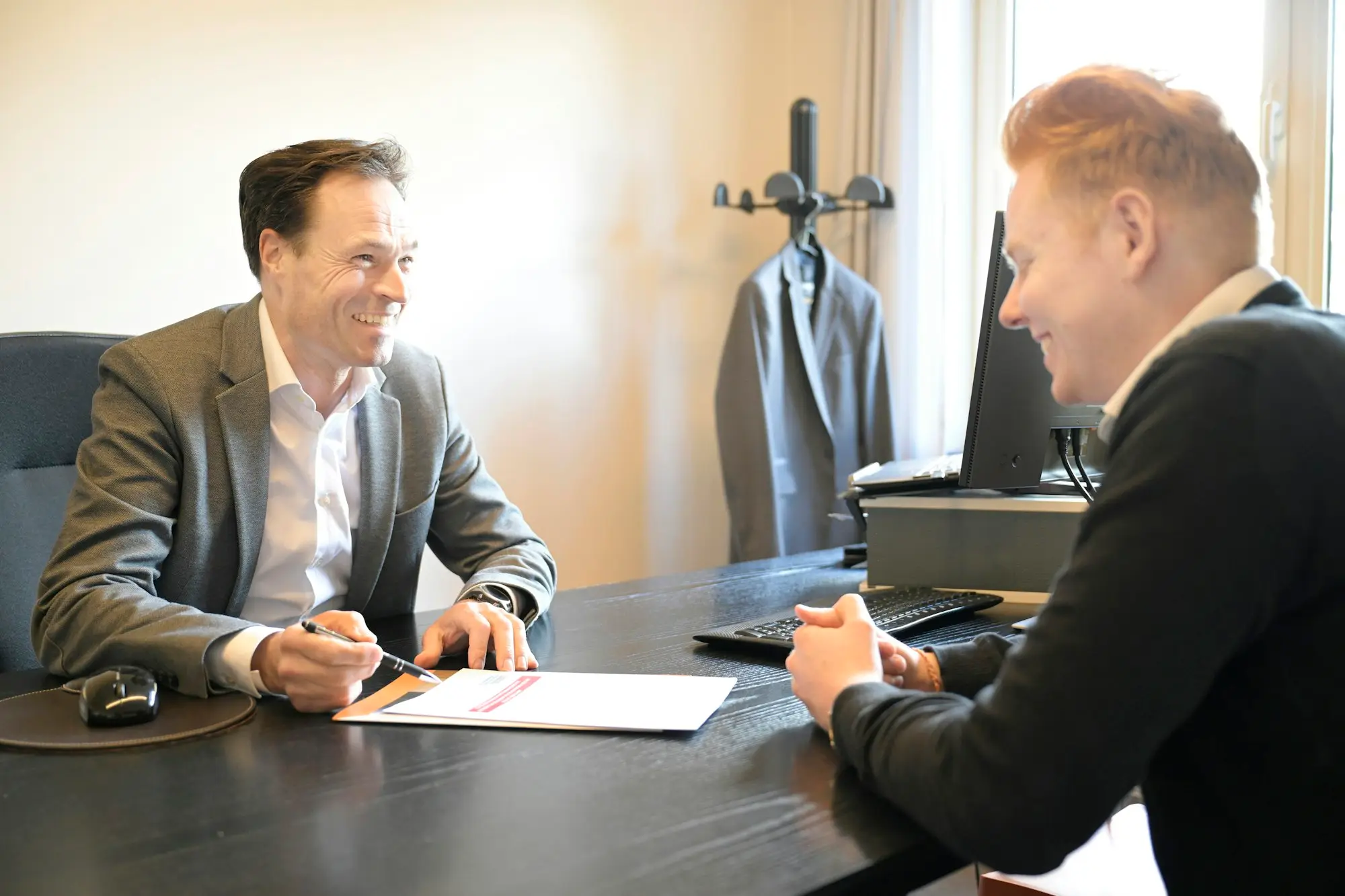 Two smiling businessmen discussing finance documents across an office desk