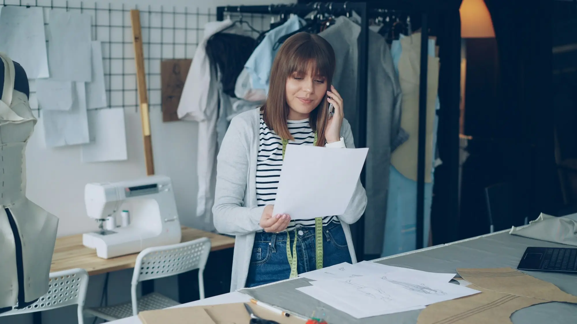Small business owner talking on her phone while reviewing designs in her clothing workshop