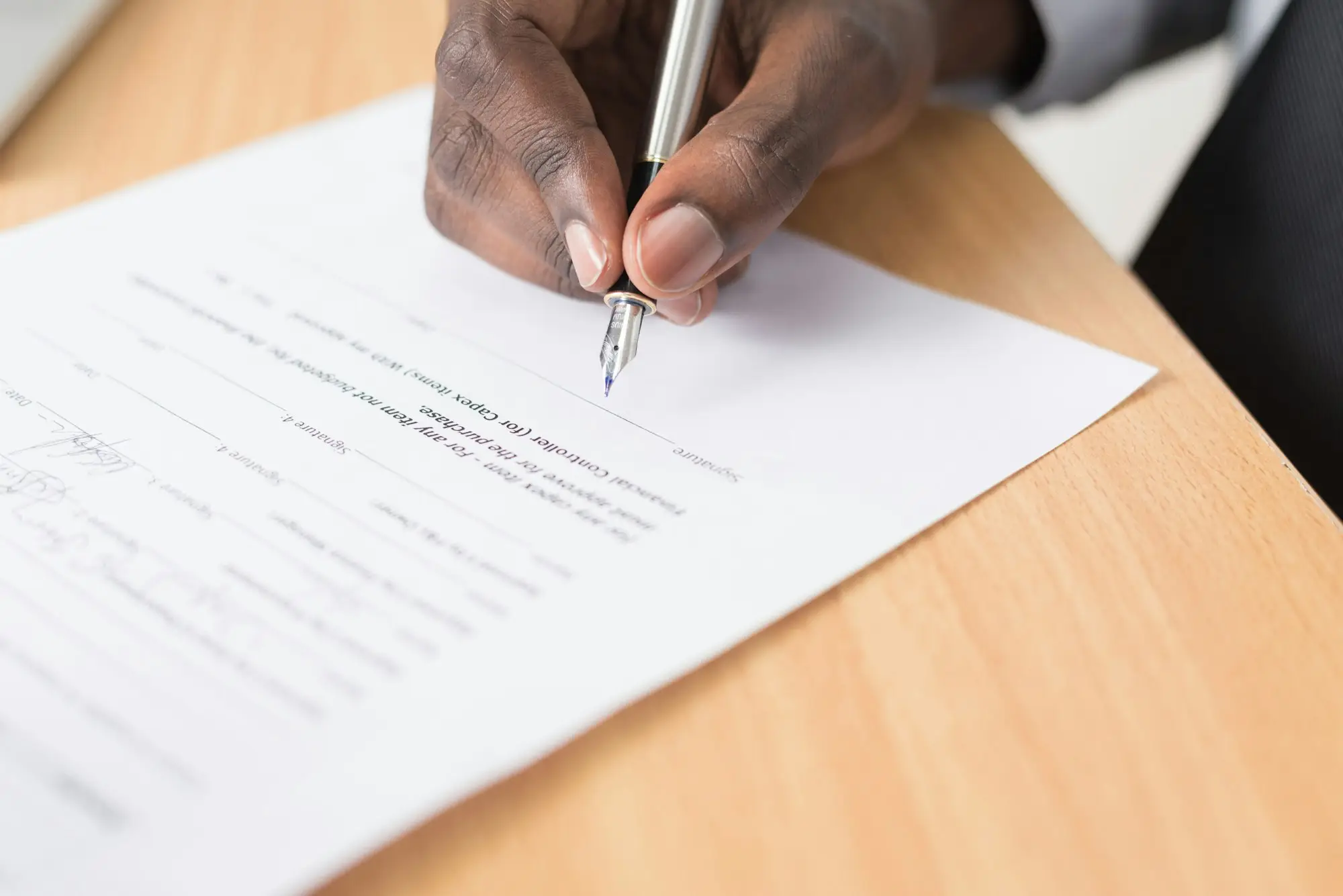 Close-up of a hand signing a loan contract with a pen at an office desk