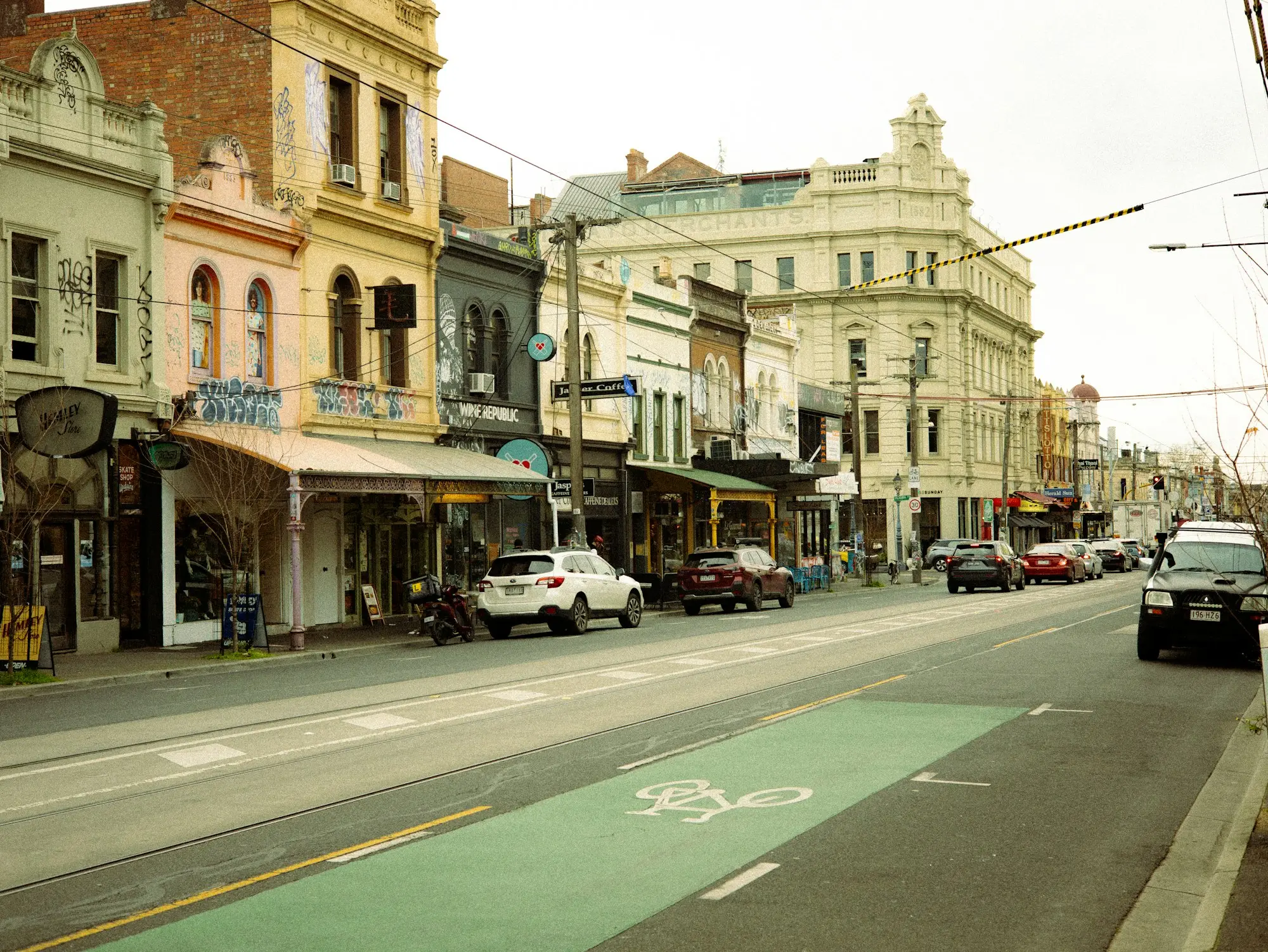 Historic Victorian shopping strip with local business shopfronts, awnings, parked cars and bike lane
